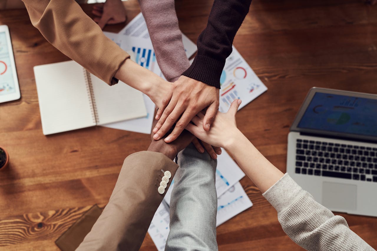 our-story Diverse professionals unite for teamwork around a wooden table with laptops and documents.